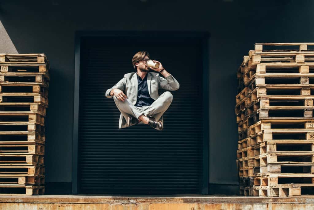 handsome young businessman floating in air in lotus pose and drinking coffee at industrial location