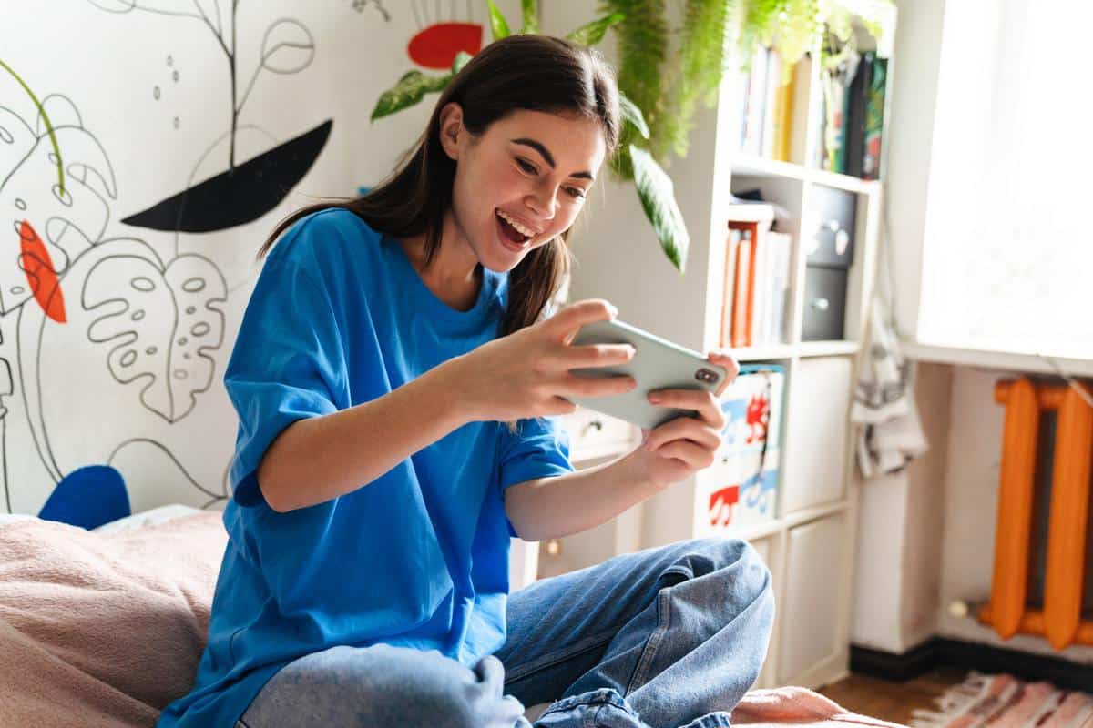 Excited girl playing online game on mobile phone while sitting on bed